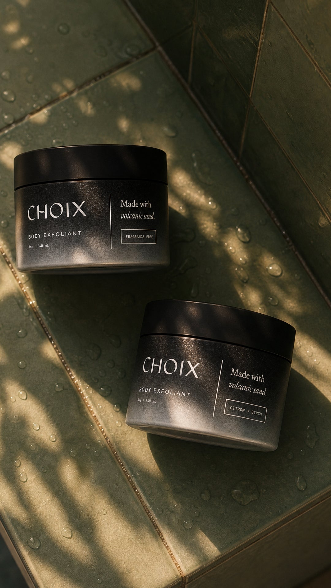 Two black jars of 'CHOIX' body exfoliant on a tiled surface with sunlight casting shadows.