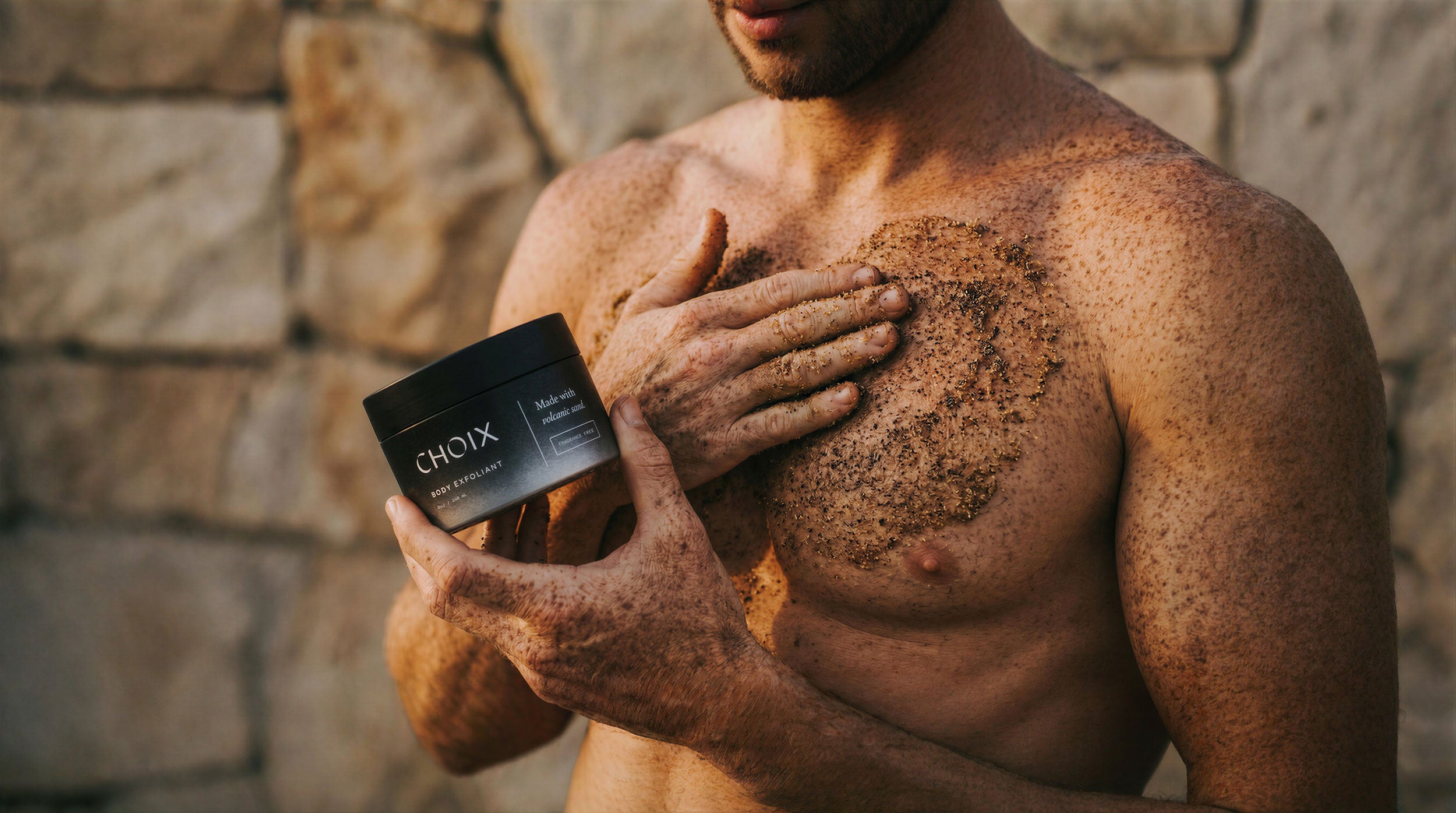 man holding a jar of CHOIX body exfoliant and applying the scrub to chest
