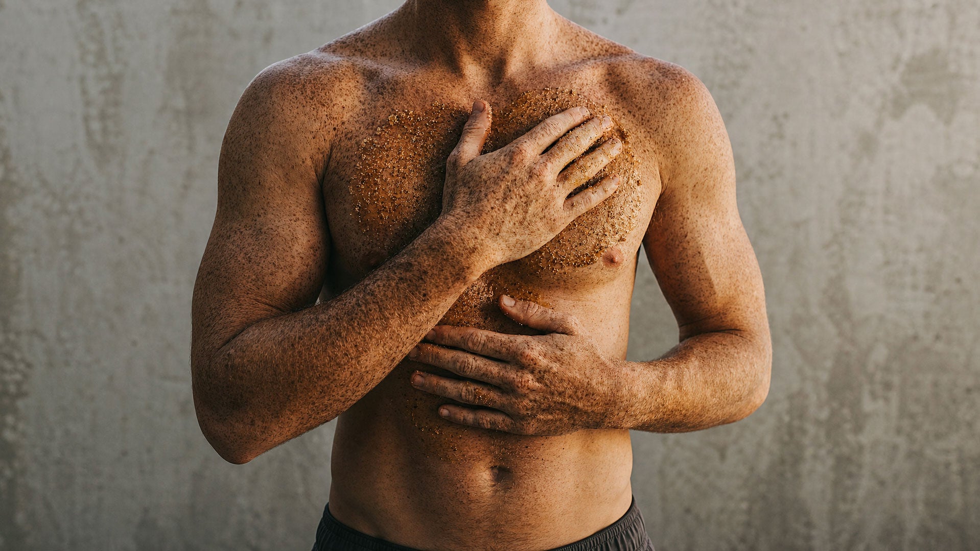 Man applying body exfoliant scrub to chest