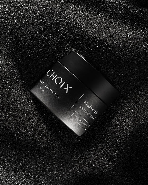 Black jar of fragrance free 'CHOIX' body exfoliant on a volcanic sand background